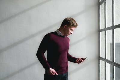 男人站在白色的混凝土墙在使用智能手机

